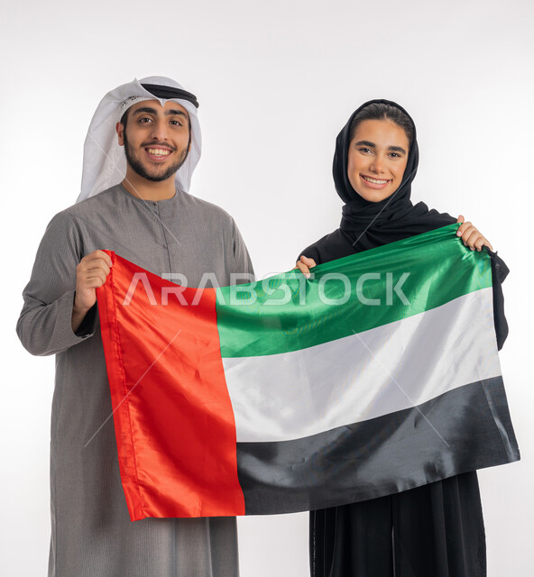 الاحتفال باليوم الوطني الإماراتي٢ ديسمبر، بورتريه لشاب وفتاة عربيان خليجيان إماراتيان مبتسمان يرتديان الزي التقليدي ويحملان بيديهما علم الإمارات ٣ نوفمبر يوم العلم الإماراتي، إيماءات الفرح والانتماء للوطن، الأعياد والمناسبات الوطنية، خلفية بيضاء، الطول الكامل للجسم