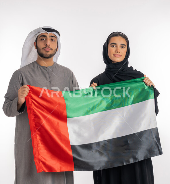 الاحتفال باليوم الوطني الإماراتي٢ ديسمبر، بورتريه لشاب وفتاة عربيان خليجيان إماراتيان مبتسمان يرتديان الزي التقليدي ويحملان بيديهما علم الإمارات، ذكرى يوم العلم الإماراتي ٣ نوفمبر، إيماءات الشموخ والافتخار بالانتماء للوطن، مناسبات وطنية إماراتية، خلفية بيضاء