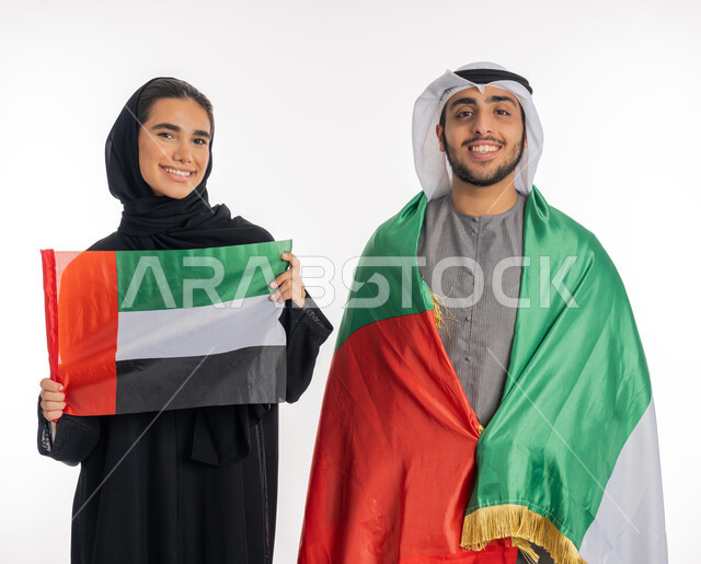 الاحتفال باليوم الوطني٢ ديسمبر، بورتريه لفتاة عربية خليجية إماراتية تحمل بيدها العلم الإماراتي وشاب عربي خليجي إماراتي يضع العلم على كتفه يرتديان الزي التقليدي، ذكرى يوم العلم الإماراتي ٣ نوفمبر، الشعور بالفخر والاعتزاز بالانتماء للوطن العربي، خلفية بيضاء