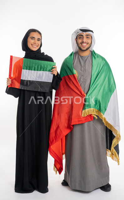 الاحتفال باليوم الوطني٢ ديسمبر، بورتريه لشاب وفتاة عربيان خليجيان إماراتيان مبتسمان يرتديان الزي التقليدي يحمل كل منهما علم دولة الإمارات، يوم العلم الإماراتي ٣ نوفمبر، الشعور بالفخر  والاعتزاز بالانتماء للوطن العربي، خلفية بيضاء، الطول الكامل للجسم