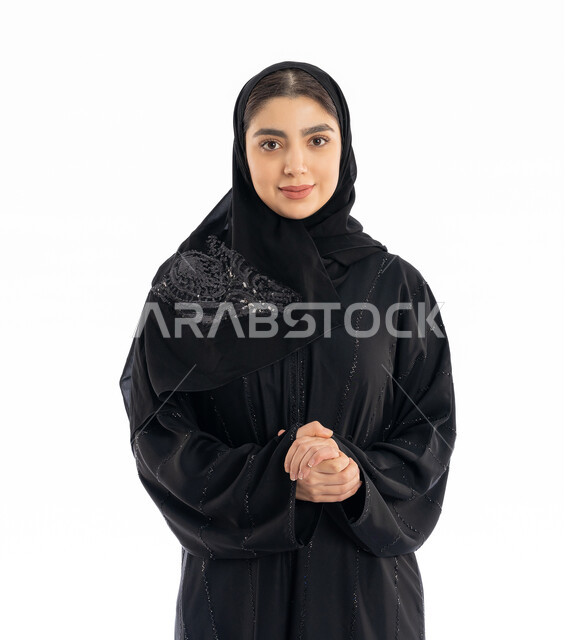 تعابير التردد في طلب شيء ما، مفهوم الأنوثة والنعومة، الاهتمام بالمظهر الخارجي، بورتريه لشابة عربية خليجية إماراتيه ترتدي العباية والحجاب تقوم بشبك يديها ببعضها، فتاة سعودية أنيقة تنظر إلى الكاميرا بإيماءات الخجل، خلفية بيضاء