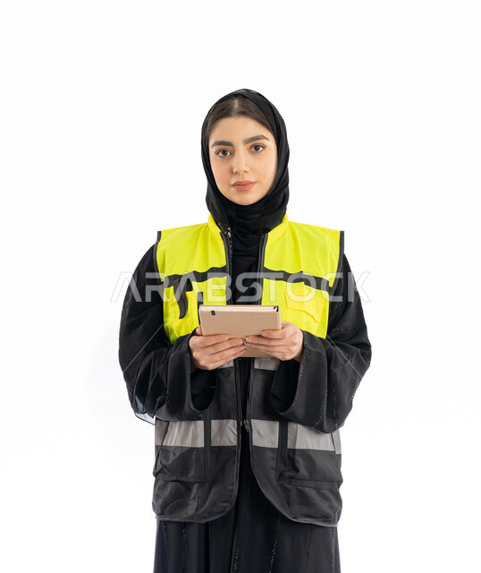 متابعة سير المشاريع، مهن ووظائف هندسية نسائية في الامارات، تدوين وتسجيل الملاحظات، بورتريه لمهندسة عربية خليجية إماراتية ترتدي العباية والحجاب وسترة الحماية تمسك بيدها دفتر صغير، شابة سعودية تنظر إلى الكامير بإيماءات الحزم والجدية، خلفية بيضاء