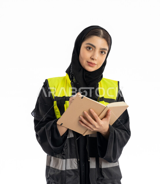 النظر إلى الكاميرا بإيماءات التركيز، متابعة سير المشاريع، مهن ووظائف هندسية في الامارات، مشاركة النساء في العمل، بورتريه مقرب لمهندسة عربية خليجية إماراتية ترتدي العباية والحجاب وسترة الحماية، شابة سعودية تقوم بتدوين ونسجيل الملاحظات، خلفية بيضاء