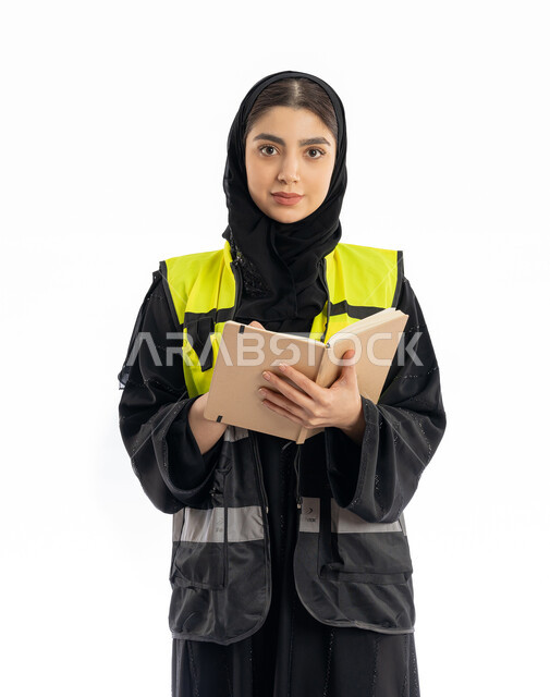 تدوين وتسجيل الملاحظات، متابعة سير المشاريع، مهن ووظائف هندسية في الامارات، مشاركة النساء في العمل، بورتريه لمهندسة عربية خليجية إماراتية ترتدي العباية والحجاب وسترة الحماية، شابة سعودية تنظر إلى الكامير بإيماءات الحزم والجدية، خلفية بيضاء