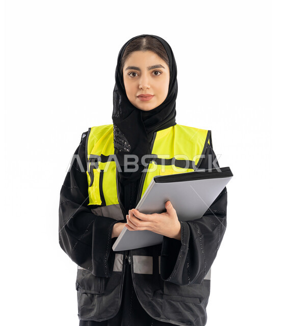 متابعة سير المشاريع، النظر إلى الكاميرا بإيماءات الحزم والجدية، مهن ووظائف هندسية في الامارات، مشاركة النساء في العمل، بورتريه لمهندسة عربية خليجية إماراتية ترتدي العباية والحجاب وسترة الحماية، شابة سعودية تمسك بملف المشروع، خلفية بيضاء