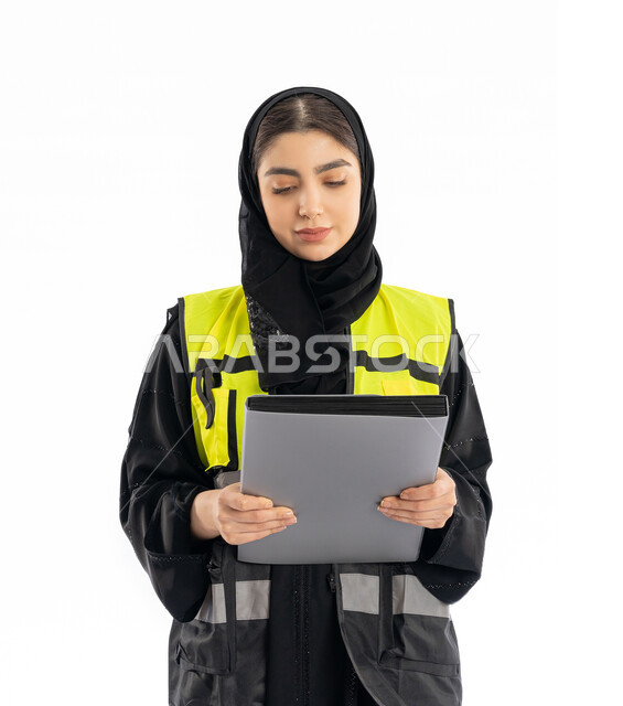 متابعة سير المشاريع، مشاركة النساء في العمل، وظائف هندسية في الامارات، بورتريه لمهندسة عربية خليجية إماراتية ترتدي العباية والحجاب وسترة الحماية، شابة سعودية تمسك بملف المشروع تنظر إليه بإيماءات  الفخر، خلفية بيضاء