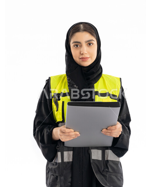 Looking at the camera with proud gestures, following the progress of projects, women's participation in work, engineering jobs in the Emirates, portrait of an Arab Gulf Emirati female engineer wearing an abaya, hijab and a protective vest, a young Saudi woman holding a project file, white background