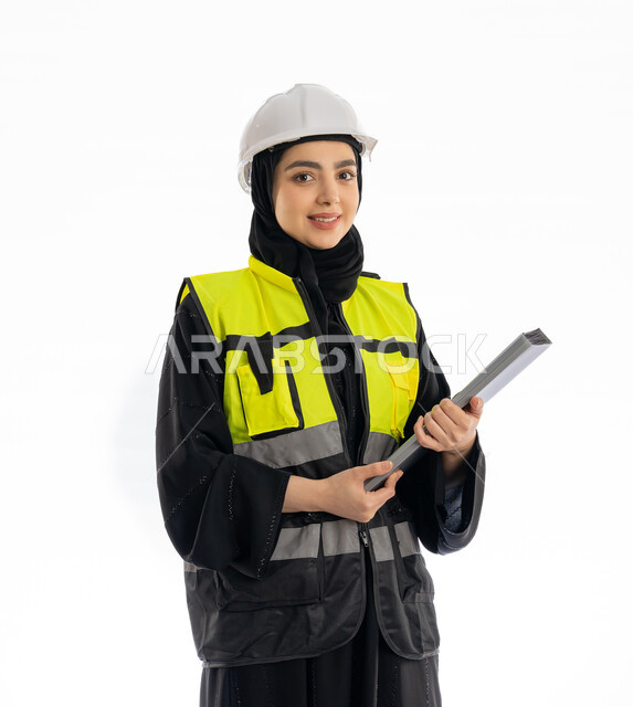 مهن ووظائف هندسية في الامارات، النظر إلى الكاميرا بإيماءات البهجة والسرور، مشاركة النساء في العمل، متابعة سير المشاريع، بورتريه لمهندسة عربية خليجية إماراتية ترتدي العباية والحجاب وسترة وخوذة الحماية، شابة سعودية تمسك ملف المشروع، خلفية بيضاء