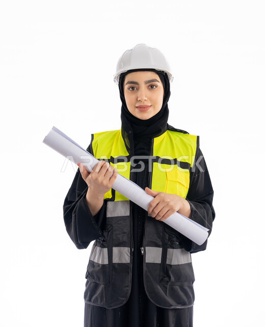 مهن ووظائف هندسيه، الإشراف على المشاريع ومتابعة سيرها، مفهوم الهندسه المعماريه, بورتريه لمهندسة عربية خليجية اماراتية ترتدي العباية وسترة وخوذة الحماية تمسك مخطط البناء, فتاة سعودية محجبة تقف باسقامة وتنظر إلى الكاميرا بإيماءات البهجة والسرور, خلفية بيضاء
