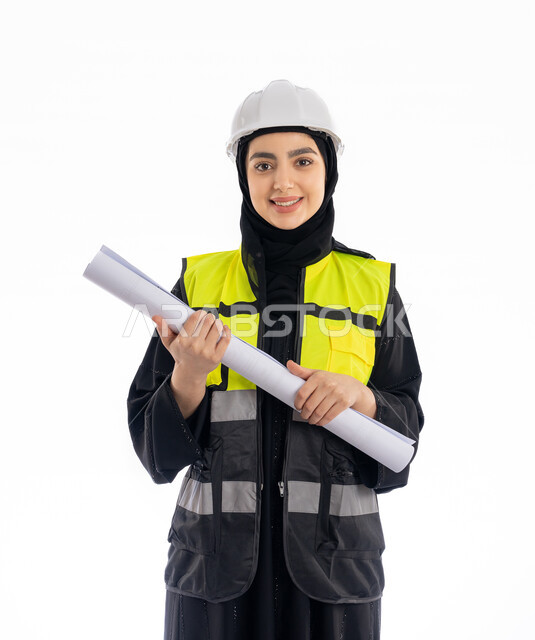 وظائف هندسيه في الإمارات، الإشراف على المشاريع ومتابعة سيرها، مفهوم الهندسه المعماريه, بورتريه لمهندسة عربية خليجية اماراتية ترتدي العباية وسترة وخوذة الحماية تمسك مخطط البناء, فتاة سعودية محجبة تقف باسقامة وتنظر إلى الكاميرا بإيماءات البهجة والسرور, خلفية بيضاء