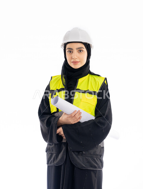 وظائف هندسيه في الإمارات، الإشراف على المشاريع ومتابعة سيرها، مفهوم الهندسه المعماريه, بورتريه لمهندسة عربية خليجية اماراتية ترتدي العباية وسترة وخوذة الحماية تمسك مخطط البناء, فتاة سعودية محجبة تقف باسقامة وتنظر إلى الكاميرا بإيماءات الحزم والجدية، خلفية بيضاء