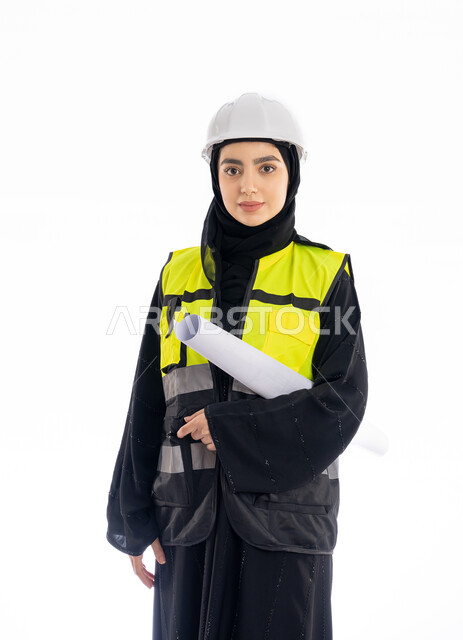 مفهوم الهندسه المعماريه, وظائف هندسيه في الإمارات، الإشراف على المشاريع ومتابعة سيرها، بورتريه لمهندسة عربية خليجية اماراتية ترتدي العباية وسترة وخوذة الحماية تمسك مخطط البناء, فتاة سعودية محجبة تقف باسقامة وتنظر إلى الكاميرا بإيماءات الحزم والجدية، خلفية بيضاء