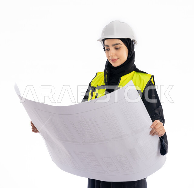 متابعة وتدقيق المخططات, بورتريه لمهندسة عربية خليجية اماراتية ترتدي العباية وسترة وخوذة الحماية تحمل بيدها مخطط البناء, فتاة سعودية محجبة تنظر إلى رسومات المشروع, مهن ووظائف هندسيه، مفهوم الهندسه المعماريه, الإشراف على المشاريع الإنشائية، خلفية بيضاء