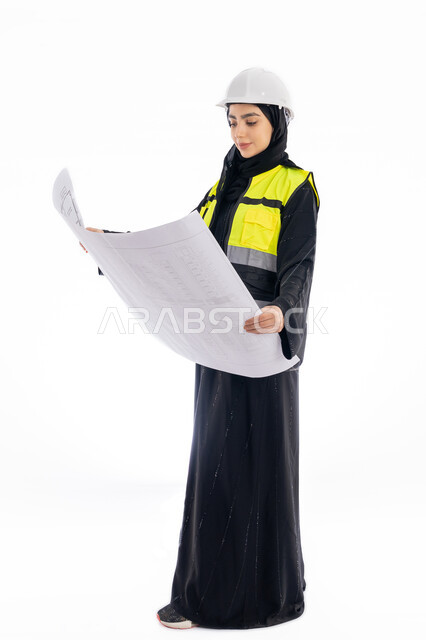مفهوم الهندسه المعماريه, الإشراف على المشاريع، متابعة وتدقيق المخططات, بورتريه لمهندسة عربية خليجية اماراتية ترتدي العباية وسترة وخوذة الحماية تحمل بيدها مخطط البناء, فتاة سعودية محجبة تنظر إلى رسومات المشروع, مهن ووظائف هندسيه، صورة لكامل الجسم، خلفية بيضاء