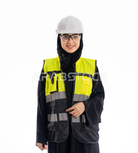 مهن ووظائف هندسية في الامارات، مشاركة النساء في العمل، متابعة سير المشاريع، بورتريه لمهندسة عربية خليجية إماراتية ترتدي العباية والحجاب وسترة الحماية، شابة سعودية تقف باستقامة وتنظر إلى الكامير بإيماءات البهجة والسرور، خلفية بيضاء