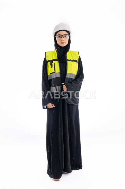 Engineering professions and jobs in the Emirates, women’s participation in the work, monitoring the progress of projects, a portrait of an Arab Gulf Emirati engineer wearing an abaya, hijab, and protection jacket, a young Saudi woman standing straight and looking at the camera with gestures of joy and pleasure, a white background.