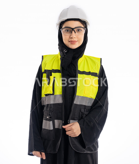 مهن ووظائف هندسية في الامارات، مشاركة النساء في العمل، متابعة سير المشاريع، بورتريه لمهندسة عربية خليجية إماراتية ترتدي العباية والحجاب وسترة الحماية، شابة سعودية تقف باستقامة وتنظر إلى الكامير بإيماءات البهجة والسرور، خلفية بيضاء