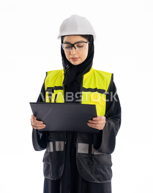 مهن ووظائف هندسية في الامارات، مشاركة النساء في العمل، متابعة سير المشاريع، بورتريه لمهندسة عربية خليجية إماراتية ترتدي العباية والحجاب وسترة الحماية، شابة سعودية تقف باستقامة وتنظر إلى الكامير بإيماءات البهجة والسرور، خلفية بيضاء