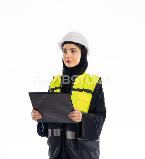 متابعة سير المشاريع، مشاركة النساء في العمل، مهن ووظائف هندسية في الامارات، بورتريه لمهندسة عربية خليجية إماراتية ترتدي العباية والحجاب وسترة ونظارات الحماية تمسك بأوراق الملاحظات الملاحظات، شابة سعودية تنظر إلى شيء ما بإيماءات التركيز، خلفية بيضاء