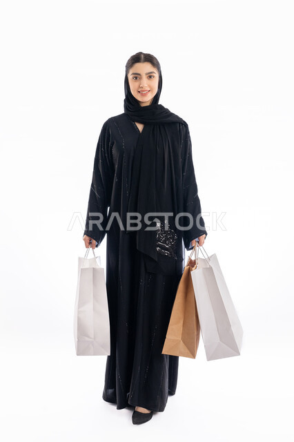 Shopping and acquisition of gifts, take advantage of performances in purchase of necessary widgets, receive online requests, a Saudi girl looking at the camera with prepare and pleasure, Portrait for Arab Gulf Arab women wearing abaya and veils stuck by bags