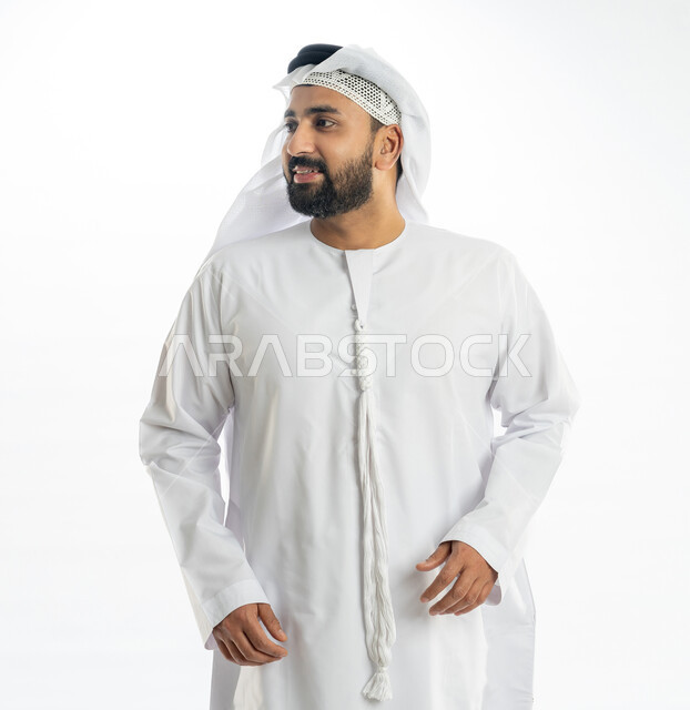 مفهوم الرجولة والقوة، الاهتمام بالمظهر الخارجي، بورتريه لرجل عربي خليجي اماراتي يرتدي الكندورة الاماراتية والغترة ينظر الى شيء ما بإيماءات البهجة والسرور، خلفية بيضاء