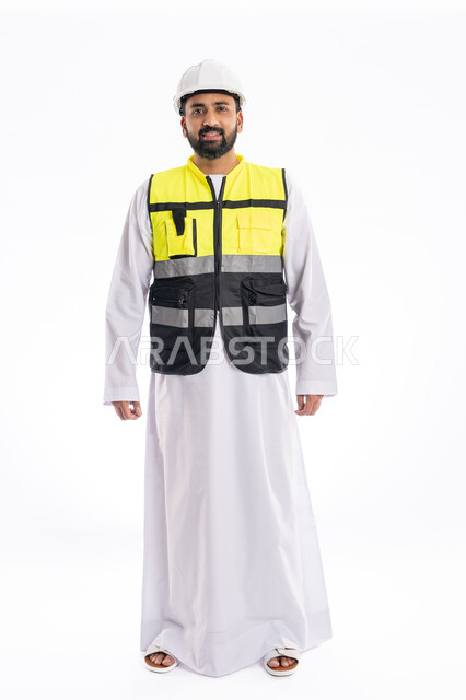 Standing straight and looking at the camera with gestures of joy and pleasure, interest in urban development by the hands of Emirati engineers, portrait of a smiling Arab Gulf Emirati engineer wearing a work jacket and a protective helmet, full body photo, white background