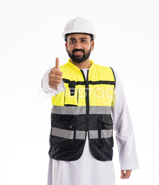 رفع اليد بإيماءات الجودة والامتياز، الوقوف باستقامة والنظر إلى الكاميرا بتعابير الرضا والقبول, الاهتمام بالتطور العمراني بسواعد المهندسين الإماراتيين، بورتريه لمهندس عربي خليجي إماراتي مبتسم يرتدي سترة العمل وخوذة الحماية، مهن ووظائف هندسية، خلفية بيضاء