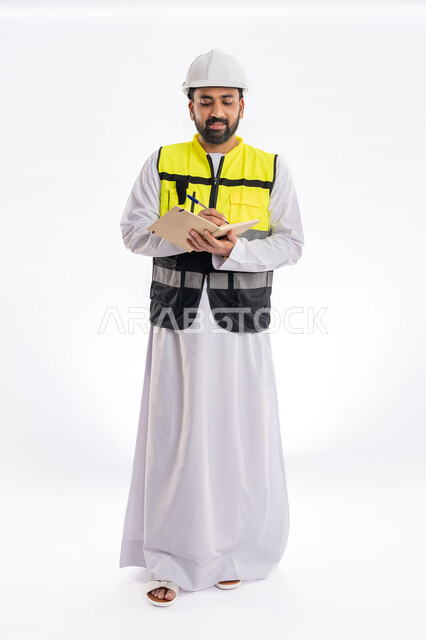 تسجيل وتدوين الملاحظات، إيماءات البهجة والسرور، الإشراف على الأعمال ومتابعة سيرها، مهن ووظائف هندسية، الاهتمام بالتطور العمراني بسواعد المهندسين في الإمارات العربية، بورتريه لمهندس عربي خليجي إماراتي يرتدي سترة العمل وخوذة الحماية، صورة لكامل الجسم، خلفية بيضاء