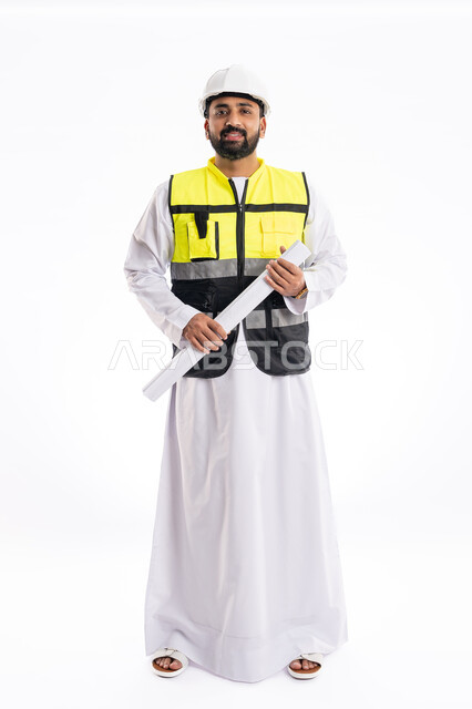 Standing straight and looking at the camera with confident gestures, engineering jobs and professions in the UAE, portrait of an Arab Gulf Emirati engineer wearing a work safety jacket and helmet holding an engineering drawing, checking and supervising project plans, full body photo, white background