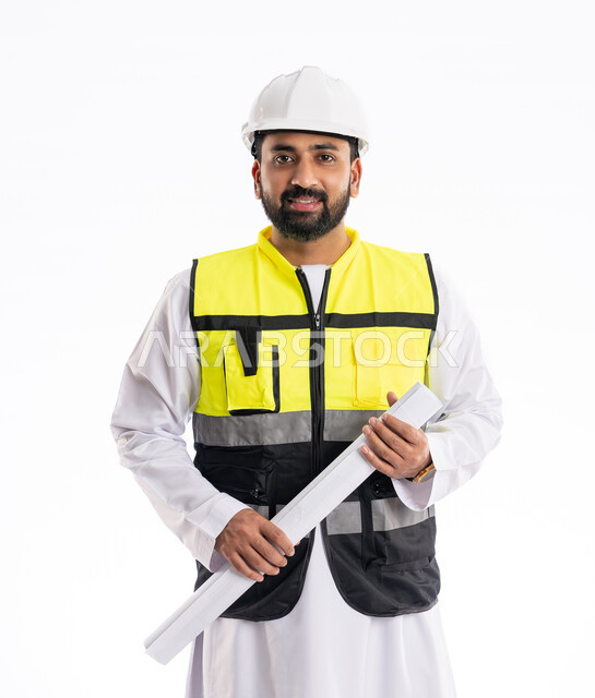 مهن ووظائف هندسية في الإمارات العربية المتحدة، النظر إلى الكاميرا بتعابير الثقة بالنفس، بورتريه لمهندس شاب عربي خليجي اماراتي يرتدي الكندورة وسترة وخوذة الحماية الخاصة بالعمل يمسك بيده مخطط هندسي، التدقيق والإشراف على مخططات المشروع، خلفية بيضاء