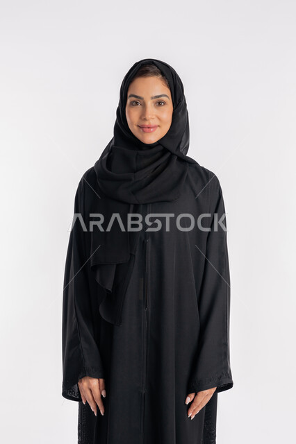 مفهوم الأناقة والاهتمام بالمظهر الخارجي، شابة سعودية تقوم بالتقاط صورة شخصية للوثائق الرسمية، أزياء محجبات عصرية راقية، بورتريه مقرب لامرأة عربية خليجية إماراتية محجبة ترتدي العباءة الحديثة وتنظر الى الكاميرا بإيماءات السرور و الثقة بالنفس، خلفية بيضاء