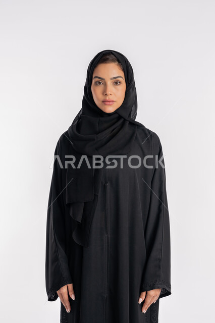 مفهوم الأناقة والاهتمام بالمظهر الخارجي، شابة سعودية تقوم بالتقاط صورة شخصية للوثائق الرسمية، أزياء محجبات عصرية راقية، بورتريه مقرب لامرأة عربية خليجية إماراتية محجبة ترتدي العباءة الحديثة وتنظر الى الكاميرا بإيماءات السرور و الثقة بالنفس، خلفية بيضاء