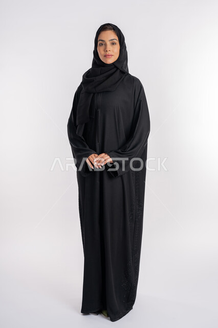 شابة سعودية تقوم بالتقاط صورة شخصية للوثائق الرسمية، أزياء محجبات عصرية، مفهوم الأناقة والاهتمام بالمظهر الخارجي، بورتريه لامرأة عربية خليجية إماراتية محجبة ترتدي العباءة الحديثة وتنظر الى الكاميرا بإيماءات السرور و الثقة بالنفس، صورة الجسم بالكامل، خلفية بيضاء