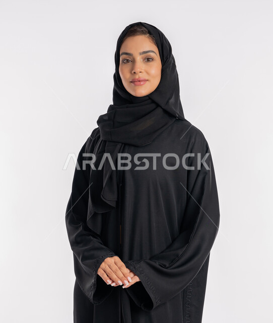 مفهوم الأناقة والاهتمام بالمظهر الخارجي، شابة سعودية تقوم بالتقاط صورة شخصية للوثائق الرسمية، أزياء محجبات عصرية راقية، بورتريه مقرب لامرأة عربية خليجية إماراتية محجبة ترتدي العباءة الحديثة وتنظر الى الكاميرا بإيماءات السرور و الثقة بالنفس، خلفية بيضاء