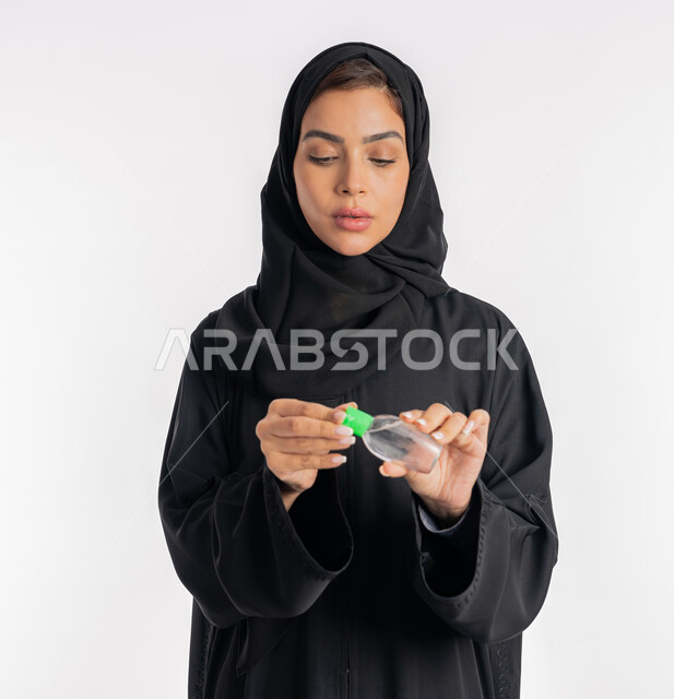 استعمال المواد الكيميائية والكحول للقضاء على الفايروسات والجراثيم، الاهتمام بالنظافة واتباع الاجراءات الوقائية من فايروس كورونا، بورتريه مقرب لإمرأة عربية خليجية إماراتية ترتدي العباءة والحجاب تمسك بيدها علبة المعقم, شابة سعودية تقوم بتعقيم يديها، خلفية بيضاء