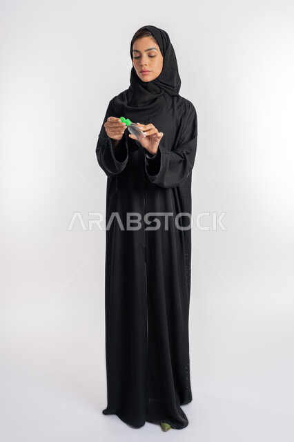 الاهتمام بالنظافة واتباع الاجراءات الوقائية من فايروس كورونا، بورتريه لإمرأة عربية خليجية إماراتية ترتدي العباءة والحجاب تمسك بيدها علبة المعقم, شابة سعودية تقوم باستخدام المواد الكيميائية والكحول للقضاء على الفايروسات والجراثيم، صورة الجسم بالكامل، خلفية بيضاء