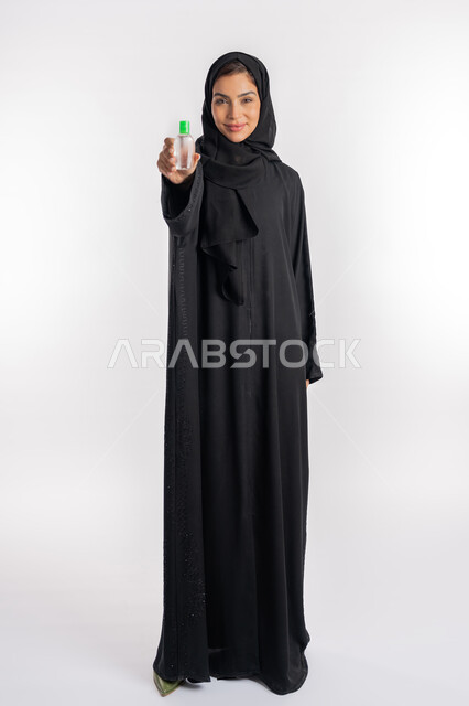 الاهتمام بالنظافة واتباع الاجراءات الوقائية من فايروس كورونا، بورتريه لإمرأة عربية خليجية إماراتية ترتدي العباءة والحجاب تمسك بيدها علبة المعقم, شابة سعودية تقوم باستخدام المواد الكيميائية والكحول للقضاء على الفايروسات والجراثيم، صورة الجسم بالكامل، خلفية بيضاء