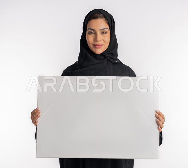 موك اب مستطيل أبيض, العروض والإعلانات التسويقية, بورتريه مقرب لإمرأة عربية خليجية إماراتية مبتسمة ترتدي الحجاب والعباءة تمسك بيديها لوحة بيضاء مستطيلة فارغة، شابة سعودية تنظر إلى الكاميرا بتعابير الفرح والسرور، لوحات توضيحية ووسائل تعليمية, خلفية بيضاء