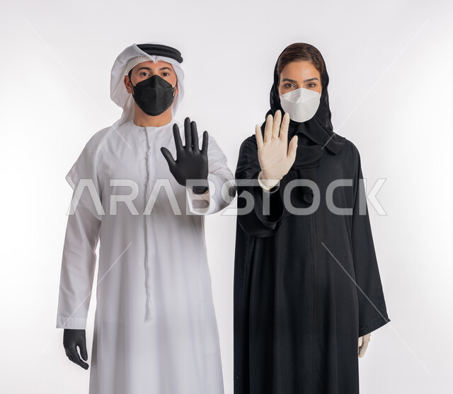 تجنب انتشار العدوى من كوفيد 19، الحفاظ على السلامة باتباع الإجراءات الاحترازية للوقاية من فايروس كورونا، الرفض ومنع الاقتراب, بورتريه مقرب لزوجين عربيين خليجيين إماراتيين يرتديان الكمامة والقفازات يرفعان كفيهما لأعلى بتعابير التحذير والتوقف, خلفية بيضاء