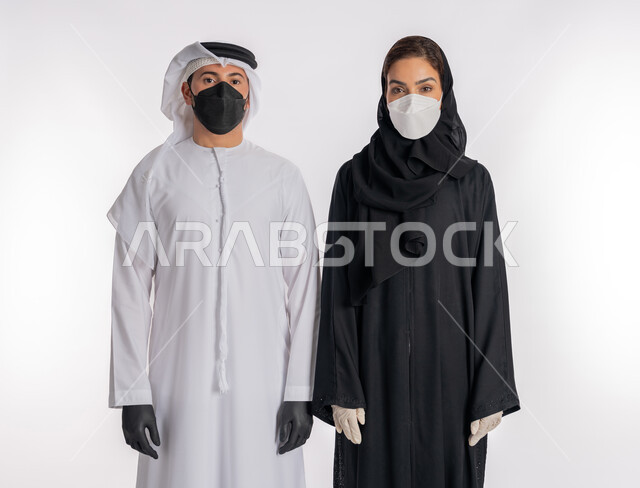 توخي الحذر من انتشار فيروس كورونا, اتباع إجراءات السلامة للوقاية من العدوى, بورتريه مقرب لزوجين عربيين خليجيين إماراتيين يرتديان القفازات والكمامة للحيطة من انتقال المرض, منع وتجنب ملامسة الايدي للجراثيم, خلفية بيضاء