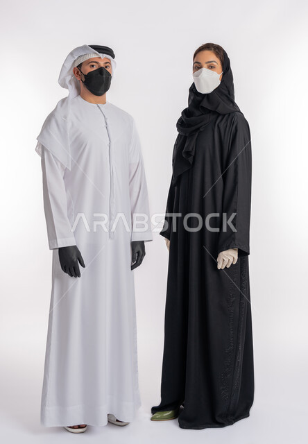 منع وتجنب ملامسة الايدي للجراثيم, توخي الحذر من انتشار فيروس كورونا, اتباع إجراءات السلامة للوقاية من العدوى, بورتريه لزوجين عربيين خليجيين إماراتيين يرتديان القفازات والكمامة للحيطة من انتقال المرض, صورة الجسم بالكامل، خلفية بيضاء