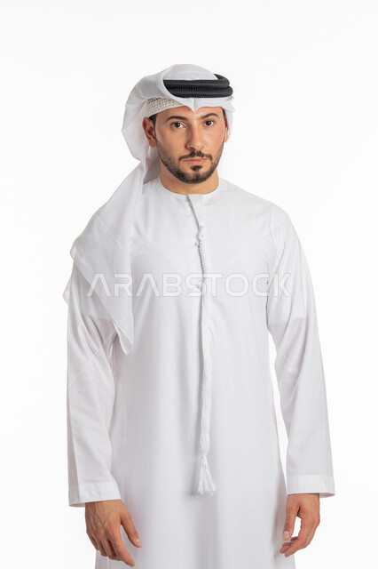 الوقوف باستعداد واستقامة، الأناقة والاهتمام بالمظهر الخارجي، التقاط الصور الشخصية للوثائق الرسمية، مفهوم الرجولة والثقة بالنفس، بورتريه مقرب لرجل عربي خليجي إماراتي يرتدي الكندورة والغترة ينظر الى الكاميرا بتعابير الحزم والجدية، خلفية بيضاء