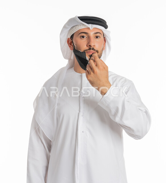 Wearing a mask to stop Covid-19 infection, Precaution against disease transmission, Following safety measures to prevent infection, Being careful against the spread of the Corona virus, Close-up portrait of an Arab Gulf Emirati man wearing a kandura and ghutra wearing a medical mask, white background