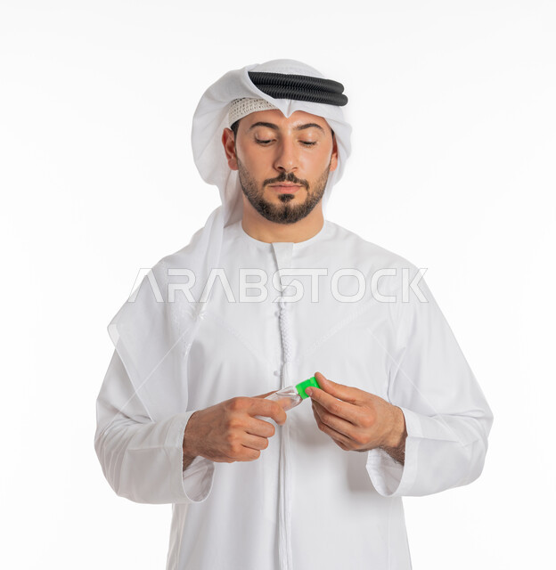 الاهتمام بالنظافة واتباع الاجراءات الوقائية من فايروس كورونا، بورتريه مقرب لرجل عربي خليجي إماراتي يرتدي الغترة والكندورة يمسك بيده علبة المعقم, استخدام المواد الكيميائية والكحول للقضاء على الفايروسات والجراثيم، خلفية بيضاء