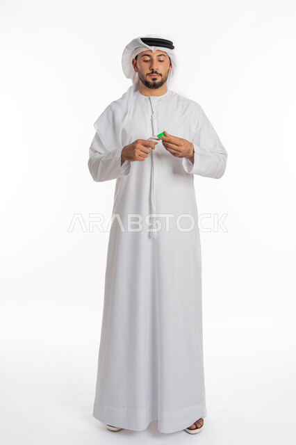 الاهتمام بالنظافة واتباع الاجراءات الوقائية من فايروس كورونا، بورتريه لرجل عربي خليجي إماراتي يرتدي الغترة والكندورة يمسك بيده علبة المعقم, استخدام المواد الكيميائية والكحول للقضاء على الفايروسات والجراثيم، صورة الجسم بالكامل، خلفية بيضاء