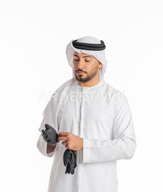 منع وتجنب ملامسة الايدي للجراثيم، اتباع إجراءات السلامة للوقاية من العدوى, توخي الحذر من انتشار فيروس كورونا, بورتريه مقرب لرجل عربي خليجي إماراتي يرتدي الكندورة والغترة يقوم بارتداء القفازات, الحيطة من انتقال المرض, خلفية بيضاء