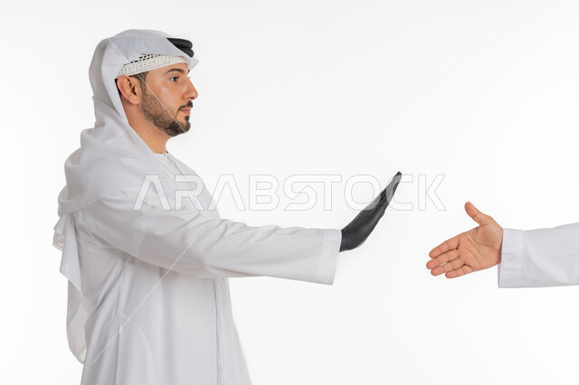 الحفاظ على المسافات وعدم الملامسه السطحيه، إتباع  الاحترازات الوقائيه ضد كوفيد 19، بورتريه مقرب من الجانب لرجل عربي خليجي اماراتي يرتدي الكندورة والغترة والقفازات للوقايه من فايروس كورونا، رفع اليد لتجنب المصافحة ومنع اقتراب الاخرين، خلفية بيضاء