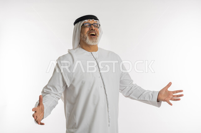 تعابير السعادة والفرح, بورتريه مقرب لرجل مسن عربي اماراتي خليجي يرتدي الكندورة و الغترة و النظارات الطبية يفتح  ذراعيه بايماءات الضحك الهستيري, حركات تدل على السرور ,قضاء وقت ممتع في العطلة, خلفية بيضاء