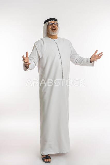 Movements indicating pleasure, expressions of happiness and joy, portrait of an elderly Arab Emirati Gulf man wearing a kandora, ghutra, and medical glasses, opening his arms with gestures of hysterical laughter, having a good time on vacation, full-length body portrait, white background