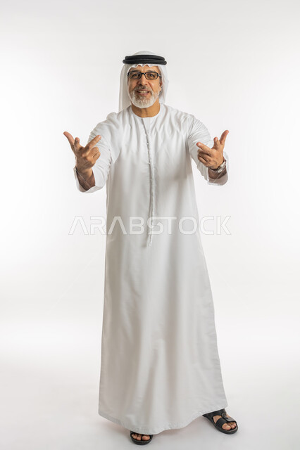 المثابرة والتميز والتحديات لتحقيق النجاح, الفوز والنصر والحب, إشارات مشعة بالأمل والتفاؤل, الوقوف باستقامة والنظر إلى الكاميرا, بورتريه لرجل كبير السن عربي خليجي إماراتي يرتدي الكندورة و الغترة يرفع يده باشارة الاصابع الثلاث, الجسم بالطول الكامل, خلفية بيضاء